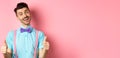 Happy smiling guy in bow-tie and suspenders showing thumbs up, praising good job, approve nice work, standing over pink Royalty Free Stock Photo