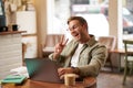 Happy smiling guy in glasses, sits in cafe, shows peace sign at laptop camera, video chats, connects to online meeting Royalty Free Stock Photo
