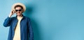 Happy smiling guy going on summer vacation, wearing straw hat and black sunglasses, standing on blue background Royalty Free Stock Photo