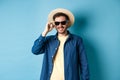 Happy smiling guy going on summer vacation, wearing straw hat and black sunglasses, standing on blue background Royalty Free Stock Photo