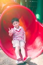 Happy smiling child showing v-sign and playing on red slider. Royalty Free Stock Photo