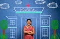 Happy smiling Indian girl kid with stethoscope standing infront of Hospital painting - concept of poor child dreaming Royalty Free Stock Photo