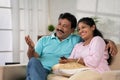 Happy smiling indian middle aged couple watching tv or television by talking each other while sitting on sofa at home - Royalty Free Stock Photo