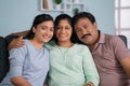 Happy smiling indian middle aged parents with adult daughter by looking at camera while sitting on sofa at home - Royalty Free Stock Photo