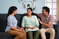 Happy smiling indian middle aged parents with daughter talking each other by looking at camera on sofa at home - concept