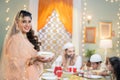 Happy smiling indian muslim woman holding seviyan kheer and sheer khurma by looking at camera in front of husband with