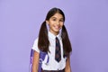 Portrait of indian schoolgirl with bag standing isolated on violet background.