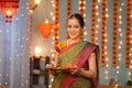 Happy smiling Indian Senior woman with Diya plate looking at camera during diwali festive celebration at home - concept