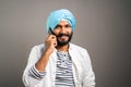 Happy smiling Indian Sikh man busy talking on mobile phone on studio background by looking camera - concept of communication, Royalty Free Stock Photo