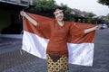 Happy smiling Indonesian woman wearing red kebaya holding Indonesia\'s flag to celebrate Indonesia Independence Day. Royalty Free Stock Photo