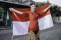 Happy smiling Indonesian woman wearing red kebaya holding Indonesia's flag to celebrate Indonesia Independence Day. Outdoor Royalty Free Stock Photo