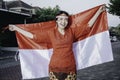 Happy smiling Indonesian woman wearing red kebaya holding Indonesia's flag to celebrate Indonesia Independence Day. Outdoor Royalty Free Stock Photo