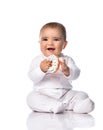 Happy smiling infant baby toddler in white onepiece jumpsuit overall sits on the floor holding donut in hands