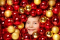 Happy Smiling Kid with Christmas Balls Toys. Child over Red and Golden Bauble Background. Shining Bright Xmas Tree Holiday Royalty Free Stock Photo