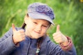 Happy smiling kid girl looking on the glass in blue clothing on summer green background. and showing the fingers cool sign. Royalty Free Stock Photo