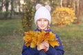 Happy smiling kid girl in a warm knitted cap collects bouquet of yellow leaves. Royalty Free Stock Photo