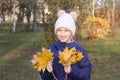 Happy smiling kid girl in a warm knitted hat collects bouquet of yellow leaves. Autumn in the park. Royalty Free Stock Photo