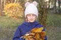 Happy smiling kid girl in a warm knitted hat collects bouquet of yellow leaves. Autumn in the park. Royalty Free Stock Photo