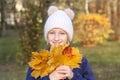 Happy smiling kid girl in a warm knitted hat collects bouquet of yellow leaves. Autumn in the park. Royalty Free Stock Photo