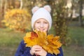 Happy smiling kid girl in a warm knitted hat collects bouquet of yellow leaves. Autumn in the park. Royalty Free Stock Photo