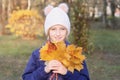 Happy smiling kid girl in a warm knitted hat collects bouquet of yellow leaves. Autumn in the park. Royalty Free Stock Photo