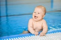 Happy, smiling little baby boy on edge of blue swimming pool in water Royalty Free Stock Photo