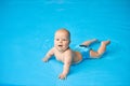 Happy, smiling little baby boy lying in blue swimming pool in water