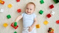 Happy smiling little baby boy lying on carpet covered with colorful toys, blocks and bricks. Concept of children Royalty Free Stock Photo