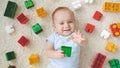 Happy smiling little baby boy lying on carpet covered with colorful toys, blocks and bricks. Concept of children Royalty Free Stock Photo