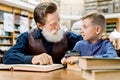 Happy smiling little boy with his cheerful bearded grandfather reading books at library, looking each other. Smiling