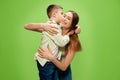 Happy, smiling little boy, son hugging and kissing his beautiful, caring mother, showing his love against green studio Royalty Free Stock Photo