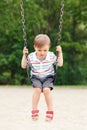 Happy smiling little boy toddler in tshirt and jeans shorts on swing on backyard playground outside Royalty Free Stock Photo