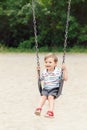 Happy smiling little boy toddler in tshirt and jeans shorts on swing on backyard playground outside Royalty Free Stock Photo