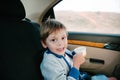 Happy smiling little boy wearing sweater holding cup of tea sitting in car near window with nature behind during automobile trip Royalty Free Stock Photo
