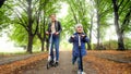 Happy smiling little boy with young mother riding on scooters on long tree alley at autumn park Royalty Free Stock Photo