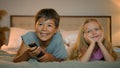 Happy smiling little caucasian children boy girl brother sister watching TV together lying on bed in bedroom kids Royalty Free Stock Photo