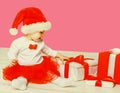 Happy smiling little child in christmas santa red hat playing with gift boxes on pink studio background Royalty Free Stock Photo