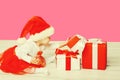 Happy smiling little child in christmas santa red hat playing with gift boxes on pink studio background Royalty Free Stock Photo