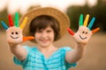 Happy smiling little girl with hands painted in funny face play outdoor in park. Focus on hands