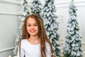 Happy smiling little girl sitting on the carpet by the Christmas tree at home waiting for gifts in the morning Royalty Free Stock Photo