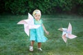 Happy smiling little girl standing on meadow and holding toy white pinwheel windmill Royalty Free Stock Photo