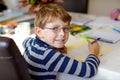 Happy smiling little kid boy with glasses at home making homework at the morning before the school starts. Little child Royalty Free Stock Photo