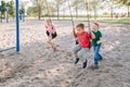 Happy smiling little preschool friends swinging on swings at playground outside on summer day. Happy childhood lifestyle concept. Royalty Free Stock Photo