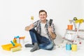 Happy smiling male sitting on floor with brush, putty knife instruments for renovation apartment room isolated on white Royalty Free Stock Photo