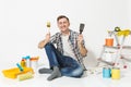 Happy smiling male sitting on floor with brush, putty knife instruments for renovation apartment room isolated on white Royalty Free Stock Photo