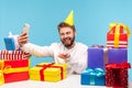 Happy Smiling Man Blogger In Cone Hat Celebrating His Birthday With Subscribers, Blowing Out Candle On Cake, Sitting At Workplace