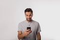 Happy smiling man in casual wear watching video on mobile phone while standing isolated in studio Royalty Free Stock Photo