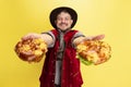 Happy smiling man dressed in traditional Bavarian costume with yummy pretzels isolated over yellow background. National