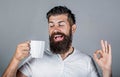 Happy smiling man holding cup of tasty fresh coffee and showing thumb up. Man holds cup of coffee, tea. Bearded man Royalty Free Stock Photo