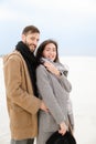 Happy smiling man hugging female person wearing grey coat and scarf, white winter monophonic background.